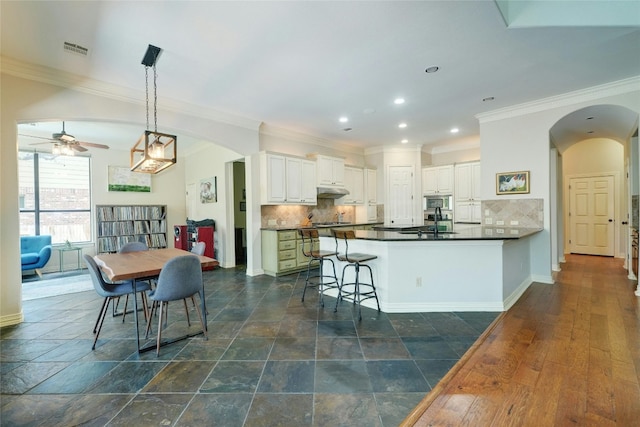 kitchen featuring backsplash, white cabinets, decorative light fixtures, kitchen peninsula, and a breakfast bar area