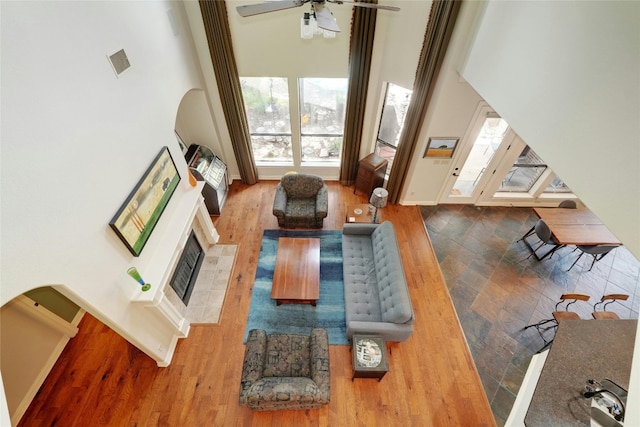 living room with a tile fireplace, ceiling fan, hardwood / wood-style floors, and a towering ceiling