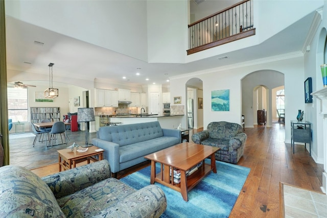 living room with ceiling fan, sink, light wood-type flooring, a tiled fireplace, and ornamental molding