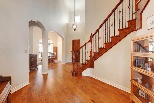 foyer entrance featuring a notable chandelier, a healthy amount of sunlight, light wood-type flooring, and a towering ceiling