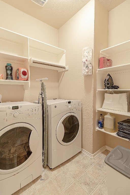 laundry area with a textured ceiling, washing machine and dryer, and light tile floors