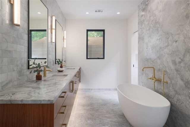 bathroom featuring tile walls, tile floors, a bath to relax in, and dual bowl vanity