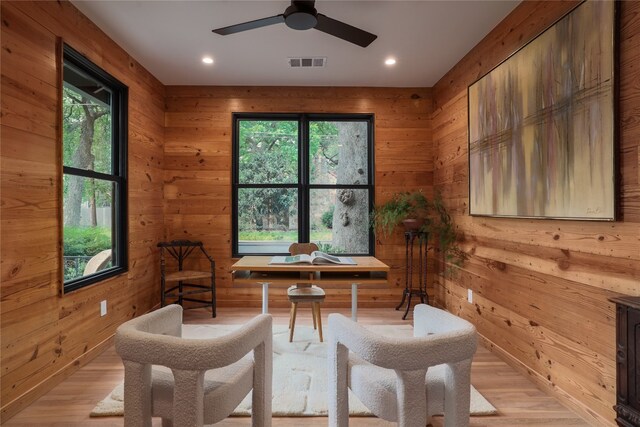 sitting room with wood walls, ceiling fan, and light hardwood / wood-style flooring