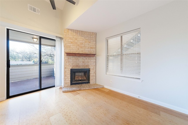 unfurnished living room with ceiling fan, hardwood / wood-style floors, a fireplace, and brick wall