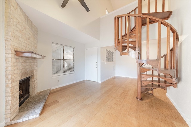 unfurnished living room with light hardwood / wood-style floors, a fireplace, brick wall, high vaulted ceiling, and ceiling fan