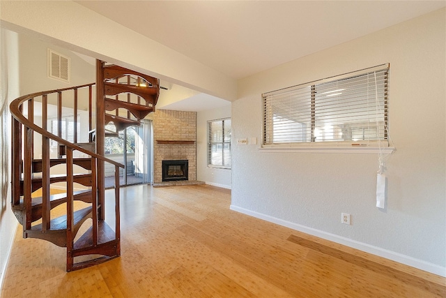 unfurnished living room with a fireplace, brick wall, and wood-type flooring