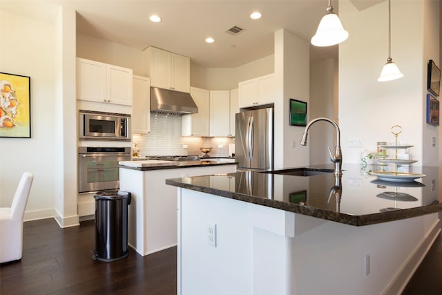 kitchen with dark hardwood / wood-style floors, a center island with sink, tasteful backsplash, white cabinetry, and appliances with stainless steel finishes