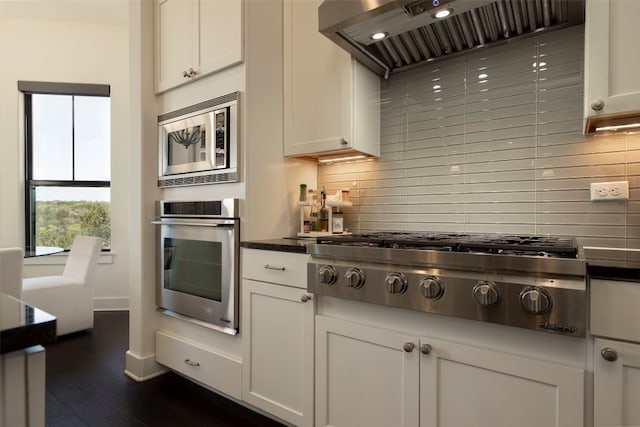 kitchen featuring wall chimney range hood, white cabinets, tasteful backsplash, and appliances with stainless steel finishes