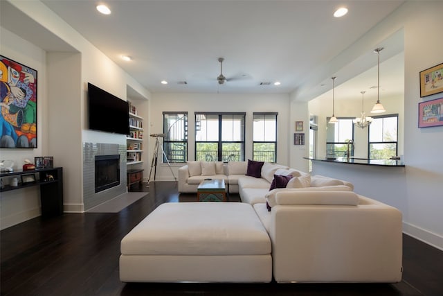 living room with dark wood-type flooring, built in features, and ceiling fan with notable chandelier