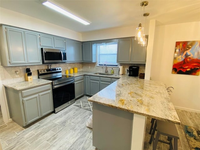 kitchen featuring kitchen peninsula, a kitchen breakfast bar, stainless steel appliances, sink, and hanging light fixtures