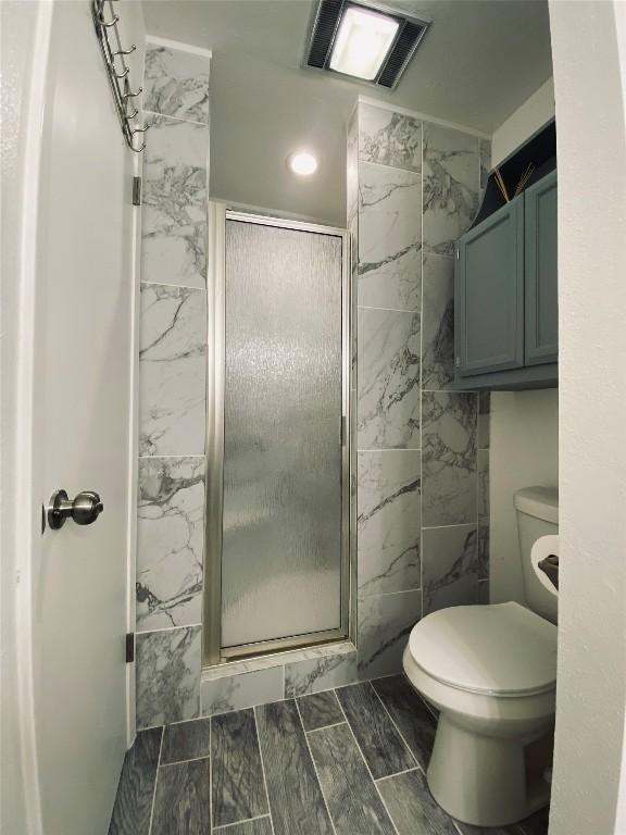 bathroom featuring a shower with shower door and toilet