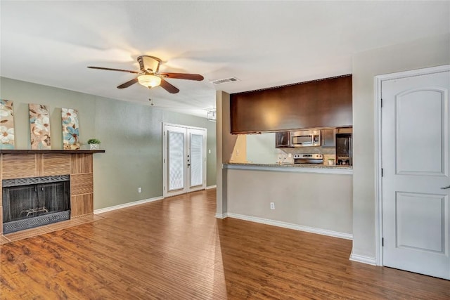 unfurnished living room with a tile fireplace, hardwood / wood-style floors, french doors, and ceiling fan