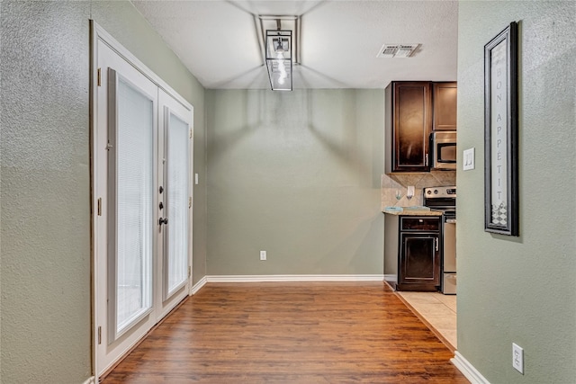 kitchen with decorative backsplash, dark brown cabinetry, appliances with stainless steel finishes, and light hardwood / wood-style flooring