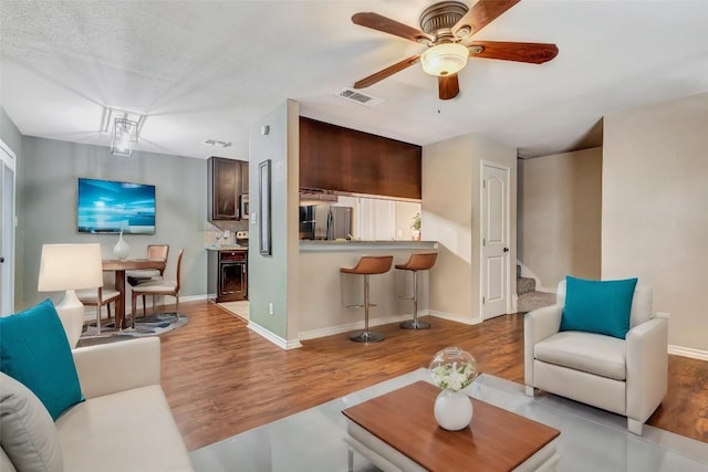 living room featuring ceiling fan, light hardwood / wood-style flooring, and a textured ceiling