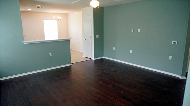 empty room with ceiling fan with notable chandelier and dark hardwood / wood-style flooring