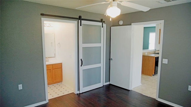 bedroom featuring wood-type flooring, a barn door, sink, ensuite bathroom, and ceiling fan