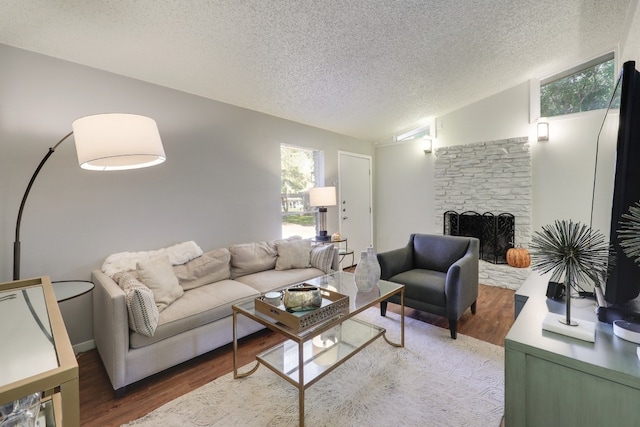 living room featuring wood-type flooring, a fireplace, vaulted ceiling, and a textured ceiling