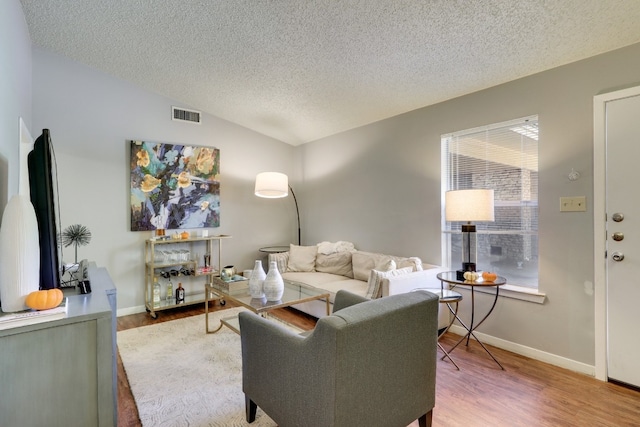 living room with vaulted ceiling, hardwood / wood-style floors, and a textured ceiling