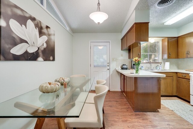 kitchen featuring a textured ceiling, light wood-type flooring, kitchen peninsula, pendant lighting, and sink