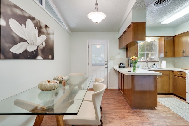 kitchen with sink, light hardwood / wood-style flooring, hanging light fixtures, a textured ceiling, and kitchen peninsula