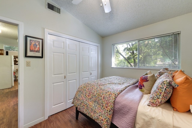 bedroom with lofted ceiling, a textured ceiling, white refrigerator, a closet, and hardwood / wood-style floors