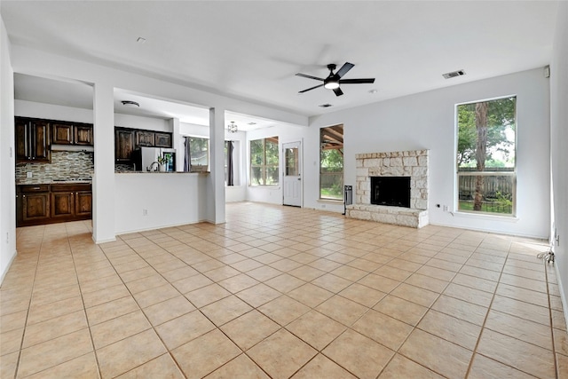 unfurnished living room featuring a stone fireplace, ceiling fan, and light tile floors