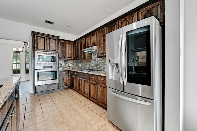 kitchen with light stone countertops, stainless steel appliances, dark brown cabinets, tasteful backsplash, and light tile floors