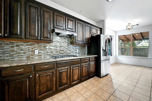 kitchen featuring light stone countertops, stainless steel appliances, backsplash, dark brown cabinetry, and light tile floors