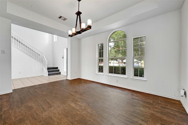 unfurnished living room with a notable chandelier, a tray ceiling, and tile floors