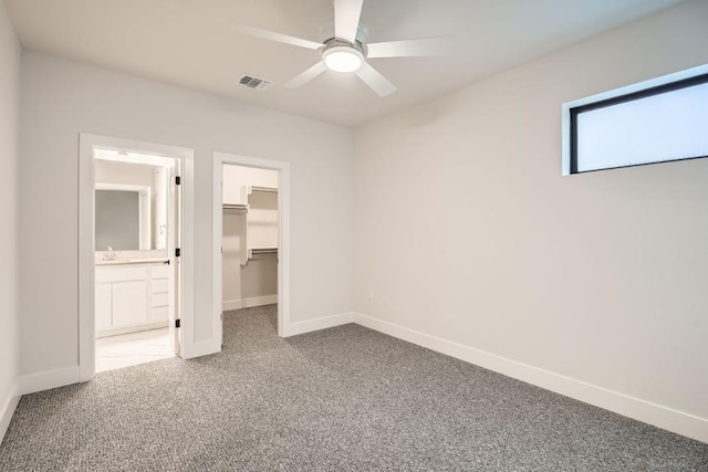 unfurnished bedroom with ceiling fan, ensuite bathroom, carpet, a walk in closet, and a closet