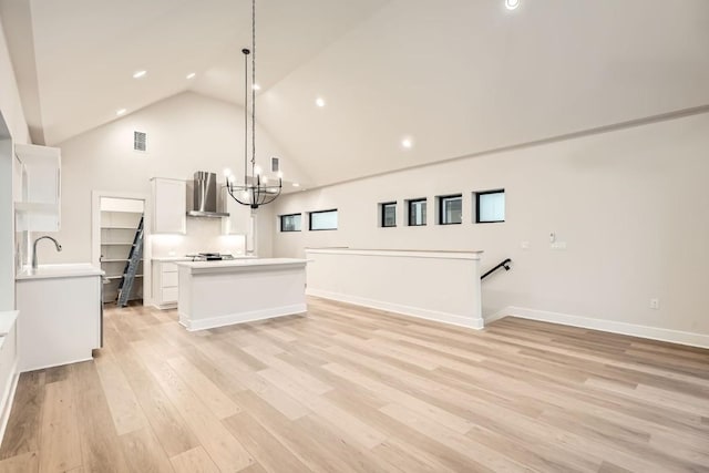 kitchen with wall chimney range hood, light hardwood / wood-style flooring, hanging light fixtures, white cabinets, and a chandelier