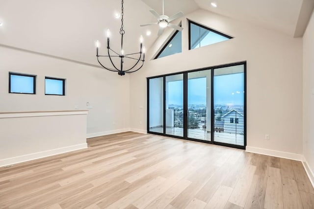 spare room with ceiling fan with notable chandelier, light hardwood / wood-style flooring, high vaulted ceiling, and a healthy amount of sunlight