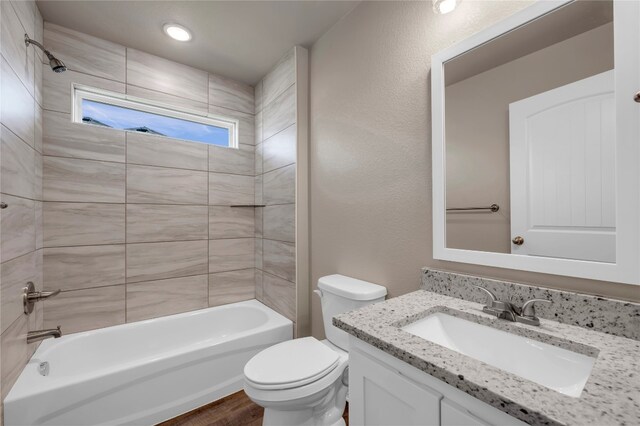 full bathroom featuring hardwood / wood-style floors, tiled shower / bath, vanity, and toilet