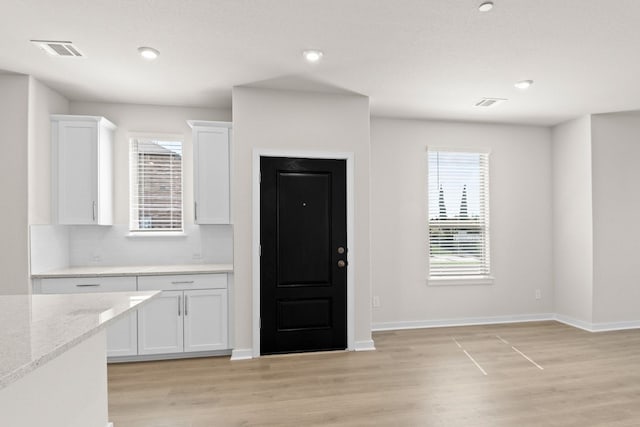 kitchen with white cabinetry, backsplash, light stone countertops, and light hardwood / wood-style flooring