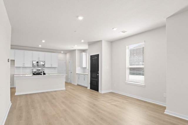 kitchen featuring decorative backsplash, a kitchen island with sink, white cabinets, appliances with stainless steel finishes, and light hardwood / wood-style floors