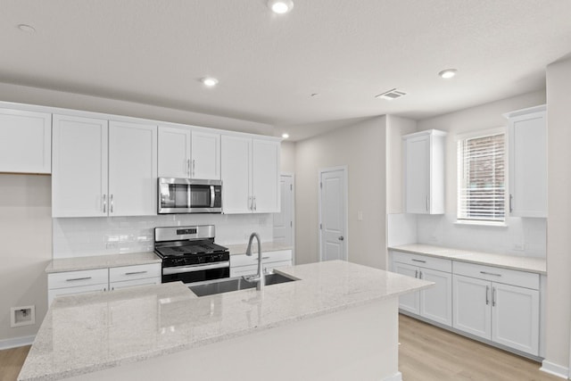 kitchen featuring light stone counters, stainless steel appliances, a center island with sink, and white cabinets