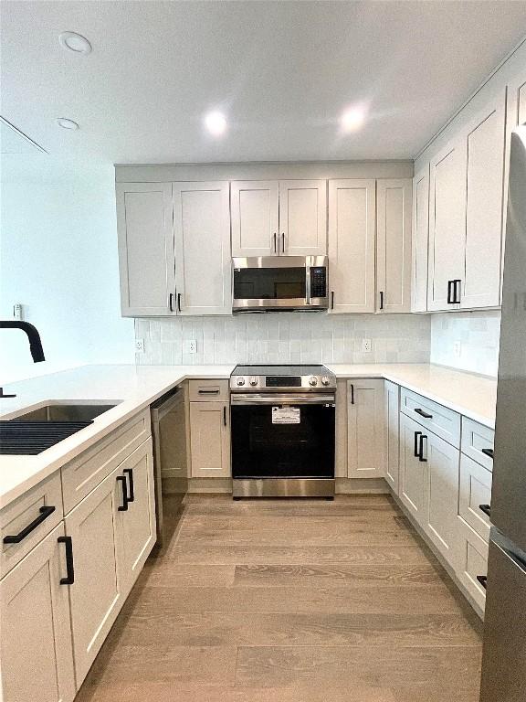 kitchen with sink, white cabinets, stainless steel appliances, and light hardwood / wood-style floors