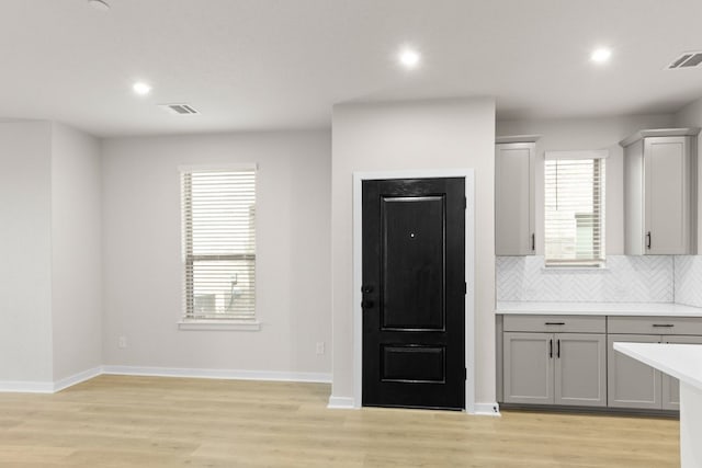 kitchen with gray cabinets, decorative backsplash, light hardwood / wood-style floors, and a wealth of natural light