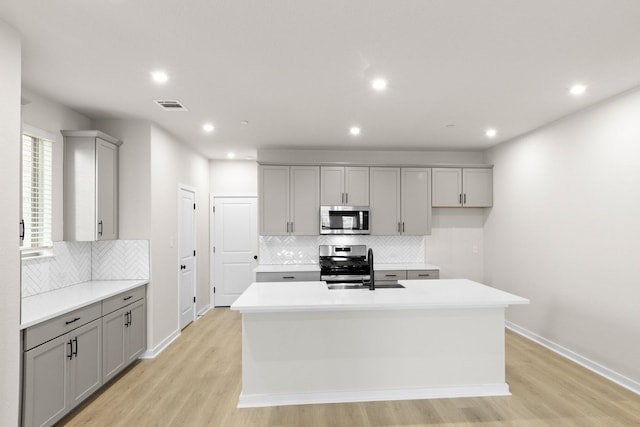 kitchen with appliances with stainless steel finishes, gray cabinetry, light wood-type flooring, and an island with sink