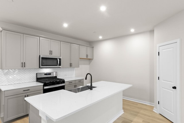 kitchen with sink, appliances with stainless steel finishes, light wood-type flooring, and an island with sink