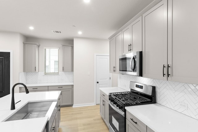 kitchen with stainless steel appliances, sink, light wood-type flooring, and gray cabinetry