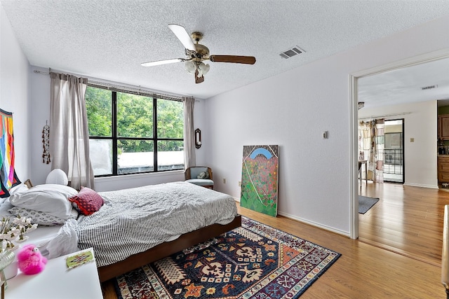 bedroom with ceiling fan, light wood-type flooring, and a textured ceiling