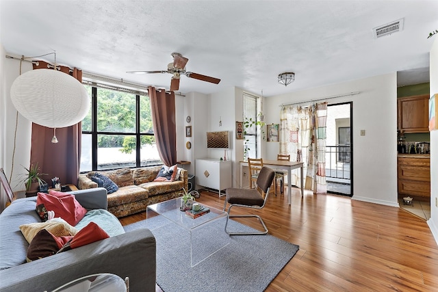 living room with a textured ceiling, light hardwood / wood-style floors, and ceiling fan