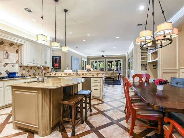 kitchen with light stone countertops, ceiling fan with notable chandelier, sink, decorative light fixtures, and an island with sink