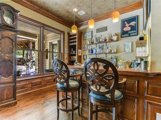 bar featuring crown molding, decorative light fixtures, and hardwood / wood-style flooring