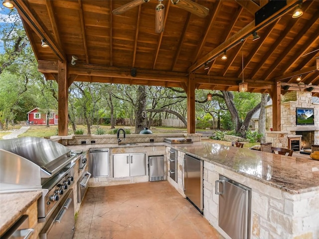 view of patio with area for grilling, an outdoor stone fireplace, ceiling fan, exterior kitchen, and a gazebo