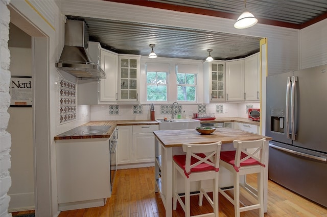 kitchen featuring stainless steel fridge with ice dispenser, decorative light fixtures, a kitchen island, wall chimney exhaust hood, and white cabinets