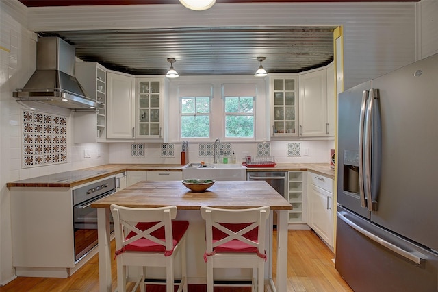 kitchen with appliances with stainless steel finishes, wooden counters, white cabinetry, sink, and range hood