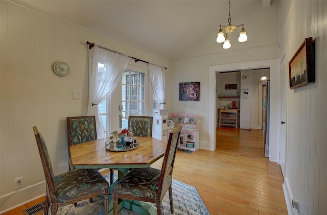 dining area with light hardwood / wood-style floors, a notable chandelier, and vaulted ceiling