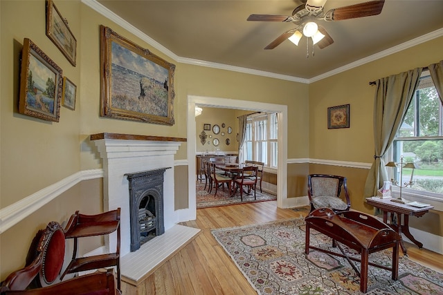 sitting room with a healthy amount of sunlight, ceiling fan, a brick fireplace, light hardwood / wood-style flooring, and crown molding